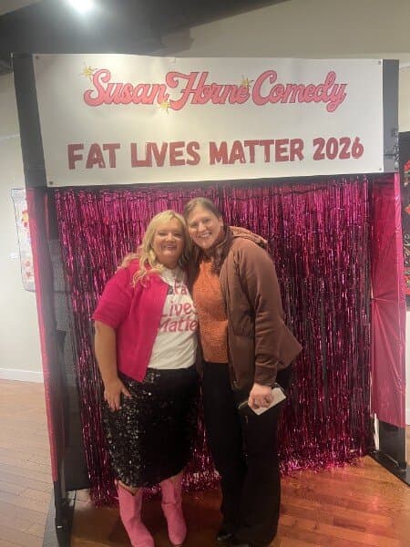 Susan with a fan in a brown jacket at the photo backdrop