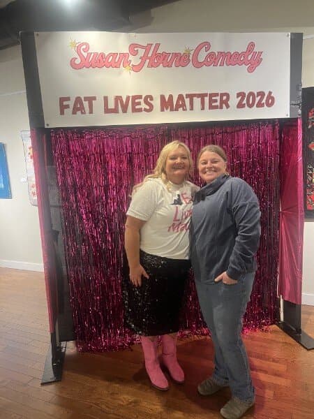 Susan posing with a fan in a blue jacket at the photo backdrop
