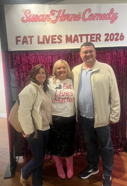 Susan between a couple at the photo backdrop, all smiling