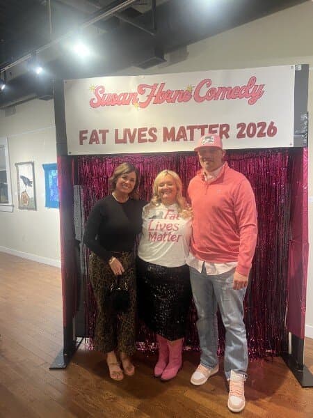 Susan with a couple, the man in a pink sweater, at the photo backdrop